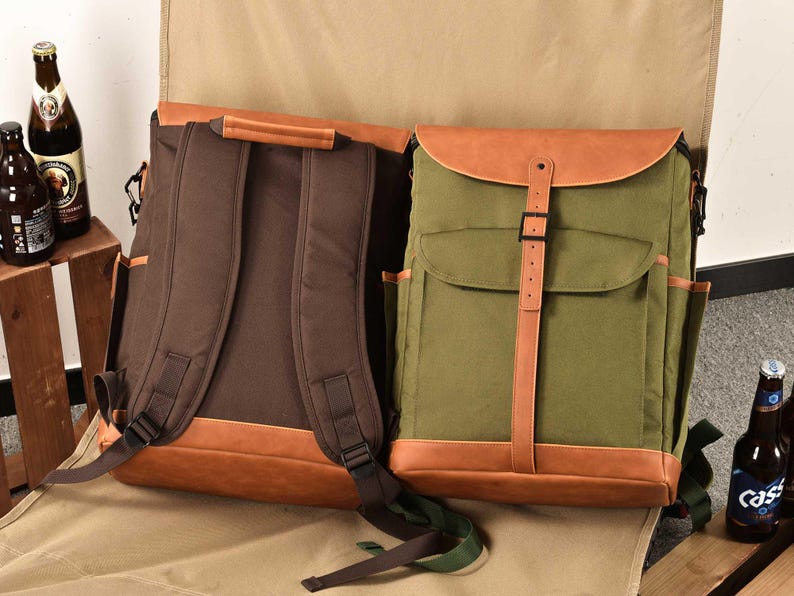 Puede incluir: Dos mochilas de lona con detalles de cuero. La mochila de la izquierda es marr&oacute;n con correas de cuero marr&oacute;n y una solapa de cuero marr&oacute;n. La mochila de la derecha es verde con correas de cuero marr&oacute;n y una solapa de cuero marr&oacute;n.
