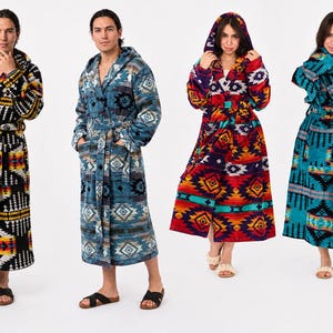 May include: Four hooded robes featuring geometric patterns in various color combinations including black, yellow, orange, blue, red, and teal. Each robe has long sleeves, a tie waist, and front pockets, showcasing distinct southwestern-inspired designs.