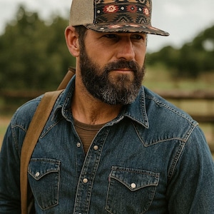 Puede incluir: Gorra de camionero con parte trasera de malla marrón y panel frontal estampado. El panel frontal presenta un diseño geométrico en tonos marrón, rojo y blanco. La gorra la lleva una persona con una camisa vaquera.