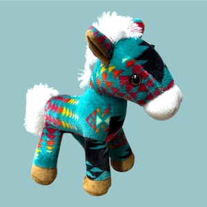 May include: A plush toy horse with a turquoise body featuring a colorful geometric pattern in red, yellow, and orange. The horse has a white mane and tail, with brown hooves and ears. The toy is standing on a light blue background.
