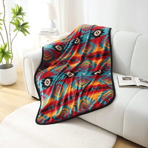 May include: A colorful blanket with a Southwestern geometric pattern in red, turquoise, orange, and black. The blanket is draped over a white sofa, showcasing its intricate design and soft texture. The blanket has a black border.