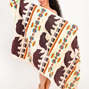 Puede incluir: Manta color crema con siluetas de osos marrones, huellas de patas de oso y patrones geométricos en naranja, turquesa y azul. La manta tiene un diseño nativo americano.