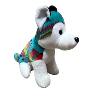 May include: A plush husky dog toy with a white body and head, and a turquoise patterned blanket. The blanket features a colorful geometric design in red, yellow, and orange. The dog has black eyes and a black nose.