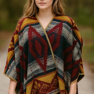 Könnte beinhalten: Ein farbenfrohes Poncho mit geometrischen Mustern in Rot, Gelb, Blau und Weiß. Der Poncho hat einen V-Ausschnitt und goldfarbene Verzierungen. Der Stil erinnert an traditionelle Webereien, mit einer warmen und einladenden Ästhetik.