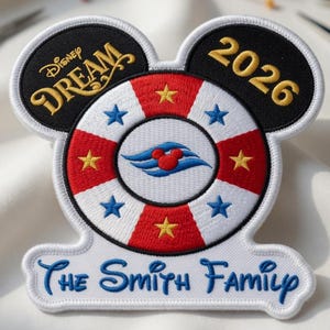 Puede incluir: Parche bordado con forma de orejas de Mickey Mouse, con el texto "Disney Dream 2026" y "The Smith Family". El diseño incluye un salvavidas con rayas rojas y blancas, estrellas azules y un icono de Mickey Mouse.