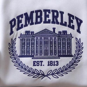 May include: A white embroidered sweatshirt with the text "Pemberley Est. 1813" in navy blue. The design features a white silhouette of a large house with columns and windows.