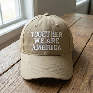 May include: A khaki baseball cap featuring the embroidered text "TOGETHER WE ARE AMERICA" in white. The cap has a curved peak and a button on top. The hat is made of a sturdy material and is suitable for everyday wear.