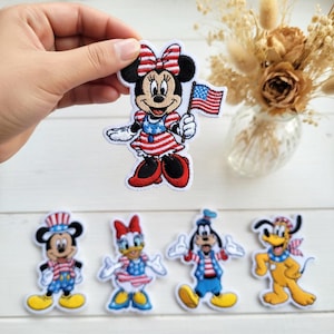 May include: Embroidered patches featuring cartoon characters in patriotic attire. Minnie Mouse holds an American flag, with Mickey Mouse, Daisy Duck, Goofy, and Pluto also in patriotic outfits. The patches are colorful with red, white, and blue designs.