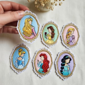 May include: Embroidered patches featuring various princess designs in oval frames with gold trim. Each patch showcases a different princess with distinct hair and attire, set against pastel backgrounds. The patches are ideal for clothing or accessory decoration.