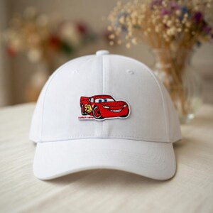 May include: A white baseball cap featuring a red cartoon car patch with the number 95. The patch has the words "custom name" below the car. The cap has a curved brim and a button on top.