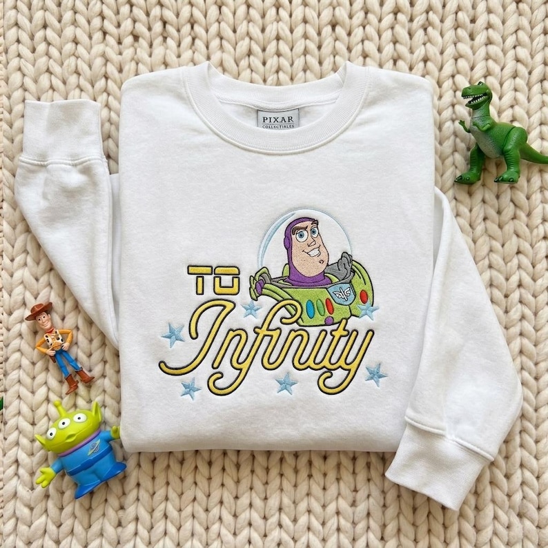 Puede incluir: Una sudadera blanca de manga larga con un bordado de Buzz Lightyear de Toy Story dentro de una burbuja, el texto "TO Infinity" en letra amarilla y peque&ntilde;as estrellas azules. Tiene una etiqueta de Pixar Collectibles en el cuello.