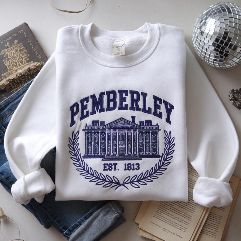 May include: White sweatshirt with a navy blue embroidered design of a building with the text "Pemberley Est. 1813" above it.