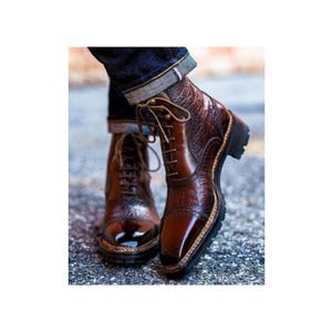 May include: Brown leather lace-up boots with a textured pattern and a pointed toe. The boots have a thick sole and a decorative stitching detail around the toe.