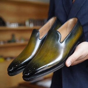Peut inclure: Une paire de chaussures &agrave; enfiler en cuir vert et noir avec une pointe pointue et un motif d&eacute;coratif sur l'avant.