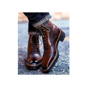 May include: Brown leather lace-up boots with a textured pattern and a pointed toe. The boots have a thick sole and a decorative stitching detail around the toe.