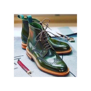 May include: A pair of green leather lace-up boots with brogue detailing. The boots have a brown leather sole and a green leather heel.