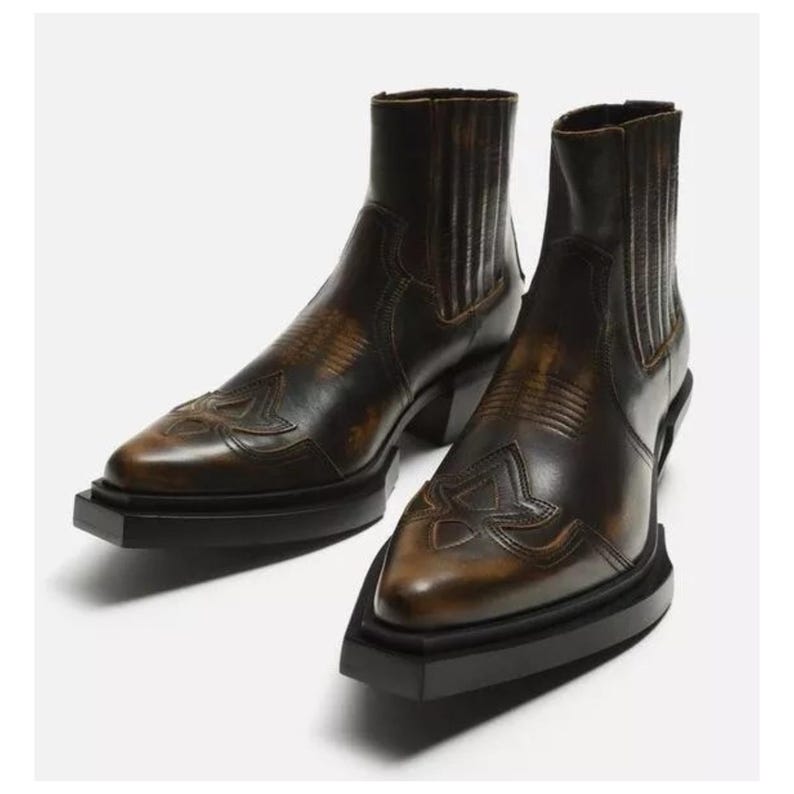 May include: A pair of brown leather ankle boots with a Western-inspired design. The boots feature decorative stitching on the toe and a block heel. The boots have a height of approximately 6 inches.