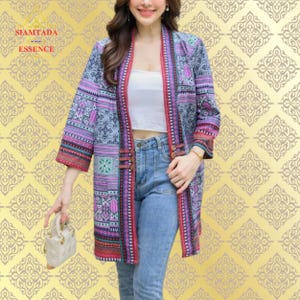 Pode incluir: Um cardigã de manga comprida estampado com um esquema de cores rosa, roxo e azul. O cardigã tem um colar de xale e fecho de botão. A modelo está usando o cardigã sobre uma blusa branca e calças de ganga azuis.