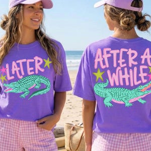 May include: Two people wearing matching violet t-shirts and shorts. The front of the shirt says "LATER" with a green alligator graphic. The back of the shirt says "AFTER A WHILE" with a green alligator graphic. The shorts are pink and white gingham.