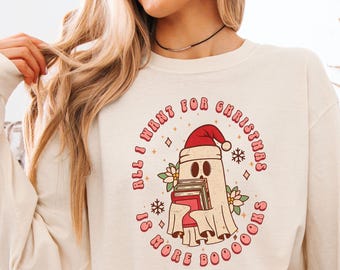 May include: Cream-colored long-sleeve shirt with the text "All I Want For Christmas Is More Boooks." The graphic features a ghost wearing a Santa hat and holding books. The words "comfort colors" are printed at the top.