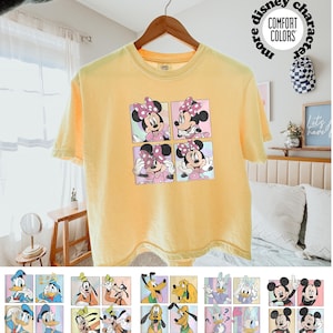 May include: Yellow t-shirt featuring a four-panel graphic of Minnie Mouse in various poses. The shirt has short sleeves and a crew neck. The text "more disney character" and "COMFORT COLORS" is printed on the shirt.