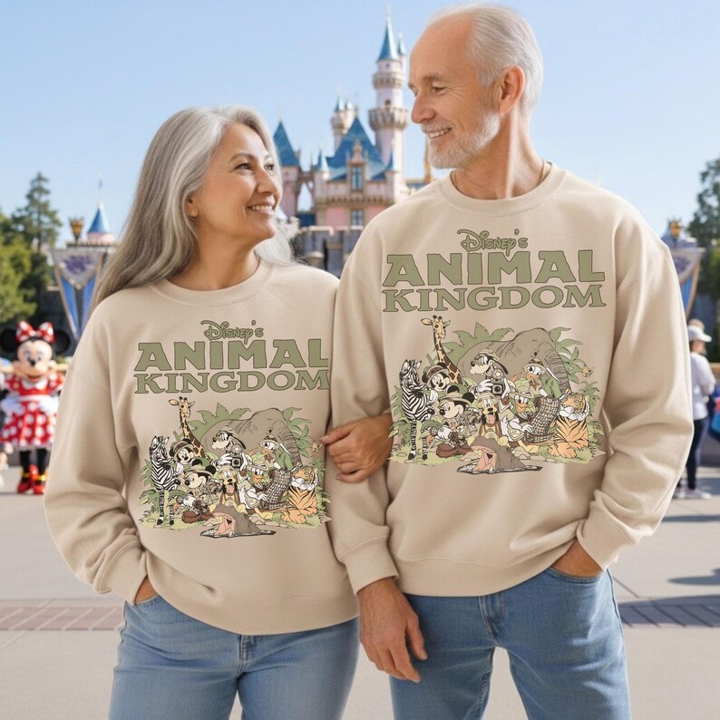 May include: Beige sweatshirts with the text "Disney's Animal Kingdom" and a graphic of various cartoon animals. The sweatshirts are worn by a couple in front of a castle and a Minnie Mouse character.