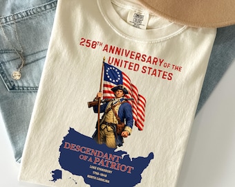 May include: Cream-colored t-shirt with a graphic commemorating the 250th anniversary of the United States. The design features a colonial soldier holding a flag, with text reading "Descendant of a Patriot" and the name Luke Stansbury.