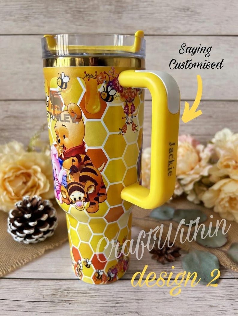 Puede incluir: Vaso t&eacute;rmico aislado amarillo y dorado con personajes de Winnie the Pooh y Tigger, con un patr&oacute;n de panal. El vaso tiene un asa amarilla con el nombre "Jackie" y el texto "Saying Customised" y "Craft Within design 2".