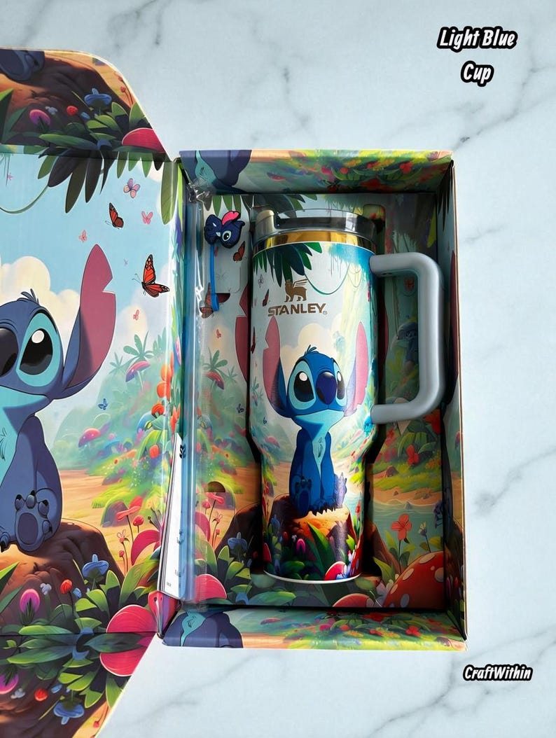Puede incluir: Una taza Stanley azul claro con un dise&ntilde;o de personaje de dibujos animados, presentada en una caja a juego. La taza tiene un asa y una tapa plateada. La caja y la taza presentan un dise&ntilde;o colorido con el texto "Light Blue Cup" y "CraftWithin".