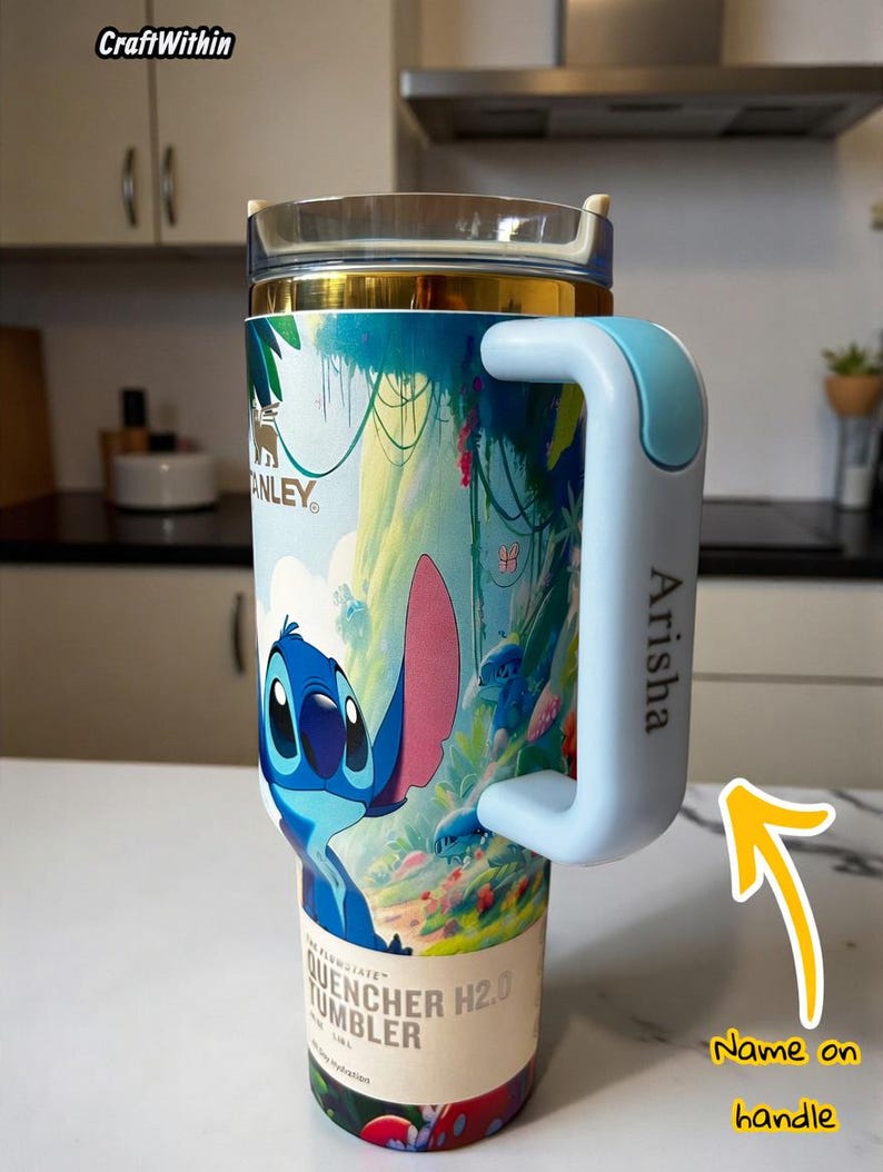 Puede incluir: Vaso t&eacute;rmico con dise&ntilde;o de Stitch. El vaso tiene un asa azul claro con el nombre "Arisha" impreso. El vaso est&aacute; etiquetado como "Quencher H2.0 Tumbler". Ideal para bebidas fr&iacute;as.