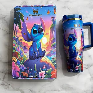 Puede incluir: Un juego de taza y caja azules con un dise&ntilde;o de personaje de dibujos animados. La caja y la taza tienen un dise&ntilde;o a juego con un personaje azul sobre una roca p&uacute;rpura con un fondo de puesta de sol. La taza tiene un asa azul y un borde plateado. La caja tiene la palabra "Stanley".