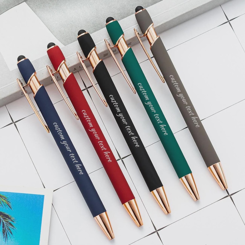 Puede incluir: Seis bol&iacute;grafos de colores con detalles dorados est&aacute;n dispuestos en diagonal. Cada bol&iacute;grafo tiene un color diferente: azul marino, rojo, negro, verde y gris. El texto "custom your text here" est&aacute; impreso en cada bol&iacute;grafo. Los bol&iacute;grafos est&aacute;n sobre una superficie blanca.