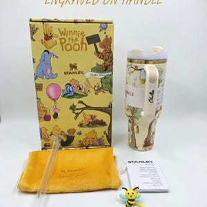 Puede incluir: Un vaso Stanley H2.0 con tem&aacute;tica de Winnie the Pooh con una caja de regalo, pajita y accesorios a juego. El vaso es de color crema con asa y tapa. La caja de regalo presenta ilustraciones de los personajes de Winnie the Pooh. Tambi&eacute;n se incluye un accesorio amarillo con forma de abeja.