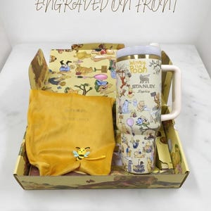 Puede incluir: Un juego de regalo tem&aacute;tico de Winnie the Pooh. El juego incluye un vaso Stanley con un asa blanca, una bolsa de terciopelo amarillo y una caja decorativa. El vaso est&aacute; cubierto de ilustraciones de los personajes de Winnie the Pooh. La caja y la bolsa son amarillas.
