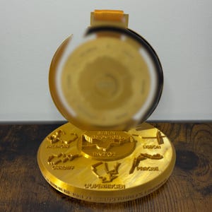 Peut inclure: Médaille dorée avec un design circulaire, avec des noms de villes comme Berlin et Cardiff. La médaille a un ruban et le texte "SUPERHALFS FINISHER". Il s'agit probablement d'un objet commémoratif pour un événement de course.