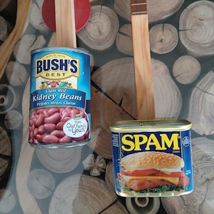 May include: Two wooden stringed instruments with red accents and a can of Bush's Best Light Red Kidney Beans and a can of Spam Classic. The cans are blue and have images of the contents.