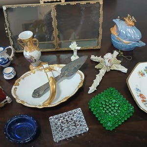May include: A collection of vintage decorative items, including a blue and white porcelain tea set, a gold-trimmed serving dish with a cake server, a blue trinket dish, and a green glass ashtray. Other items include a decorative cross and a floral plate.