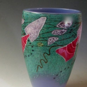 May include: A tapered glass vase featuring a vibrant teal and green speckled body with a solid lavender base and interior. The exterior is decorated with abstract purple shapes, bright pink conical forms, and thin dark brown wavy lines.