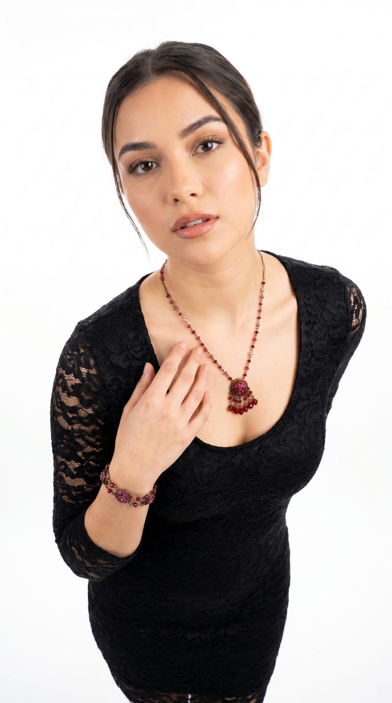 Puede incluir: Una mujer con un vestido de encaje negro y un conjunto de joyas a juego. El conjunto incluye un collar con colgante y una pulsera, ambos con piedras preciosas rojas. Fondo blanco.