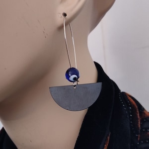 May include: Silver hoop earrings with a dark gray crescent moon charm and a blue evil eye bead.