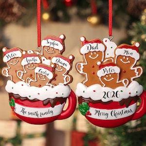May include: Two hanging Christmas ornaments shaped like red mugs filled with gingerbread figures wearing Santa hats. The left mug features the names Peter, Agatha, Sophia, Carlin, and Diana with The Smith Family text. The right mug features Dad, Mom, and Peter with 2026 and Merry Christmas text.