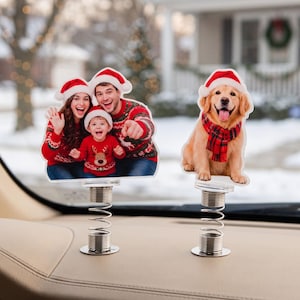 Könnte beinhalten: Zwei personalisierte Wackelfiguren mit Fotoausschnitten auf Metallfedern. Eine Figur zeigt eine dreiköpfige Familie in roten Weihnachtspullovern und Weihnachtsmannmützen. Die zweite Figur zeigt einen Golden Retriever mit rotem Schal und Weihnachtsmütze.