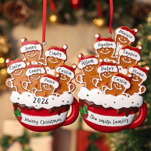 May include: Two red and white ceramic mug ornaments featuring gingerbread figures wearing Santa hats. The left mug displays the year 2026 and names Jenny, Cindy, Claire, Sandy, Peter, and Carlin. The right mug says The Smith Family with names Agatha, Maisie, Sophia, Allen, Peter, Carlin, and Diana.