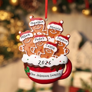 May include: A Christmas tree ornament shaped like a red mug filled with white frosting and five gingerbread figures wearing Santa hats. The figures are labeled Agatha, Maisie, Allen, Peter, Sophia, and Carlin. The mug displays 2026 and The Johnson family.