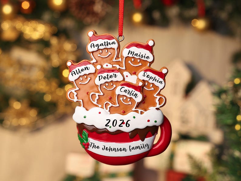May include: A Christmas tree ornament shaped like a red mug filled with white frosting and five gingerbread figures wearing Santa hats. The figures are labeled Agatha, Maisie, Allen, Peter, Sophia, and Carlin. The mug displays 2026 and The Johnson family.