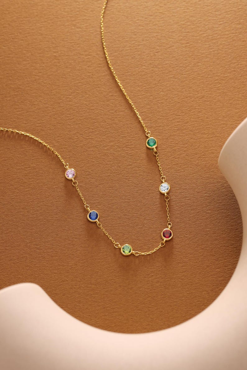 Op de afbeelding: Een gouden ketting met zes gekleurde edelstenen. De edelstenen zijn roze, blauw, groen, rood, wit en groen.