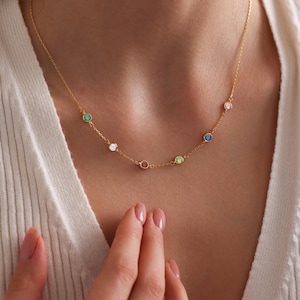 Op de afbeelding: Een gouden ketting met een rij gekleurde edelstenen. De edelstenen zijn groen, wit, rood, lichtgroen en blauw.