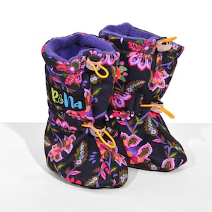 May include: A pair of black boots with a vibrant floral pattern in shades of pink, orange, and green. The boots feature a purple fleece lining, a black label with the text Rona in blue and yellow, and yellow elastic drawstrings with clear toggles.