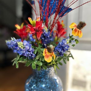 May include: A white ceramic mug with a black handle and the text "But First, Coffee" in a bold, black font. The mug is set against a blurred background, highlighting its simple design.