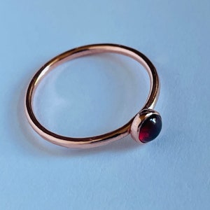 May include: A simple rose gold ring with a single red gemstone.